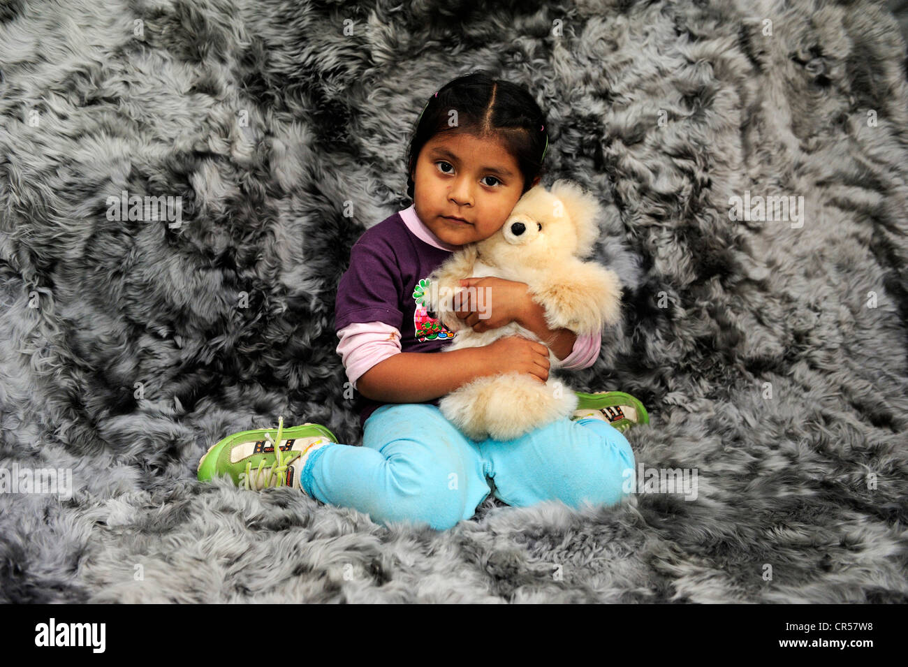 Girl with indigenous facial features hugging a teddy bear, production of soft toys and carpets from alpaca fur in a small family Stock Photo