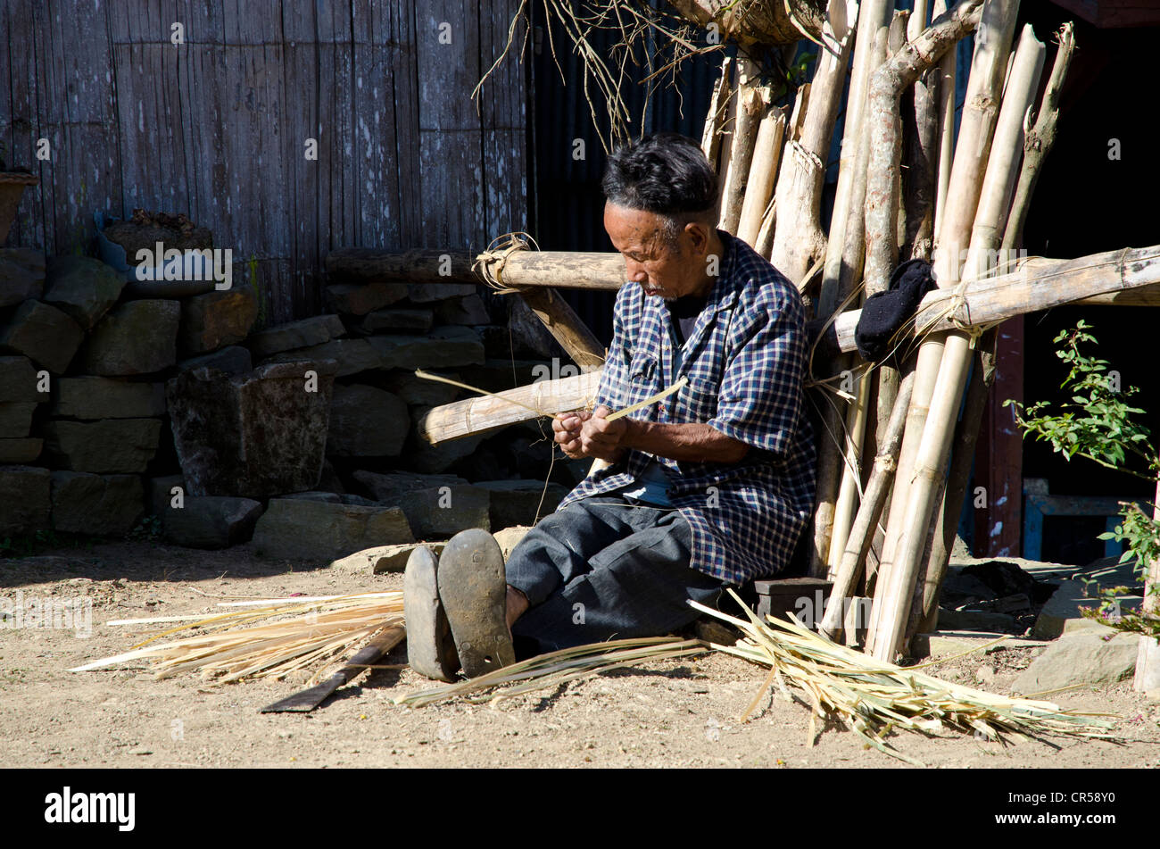 Man of the Ao tribe braiding in front of his house, Ungma village, Nagaland, India, Asia Stock Photo