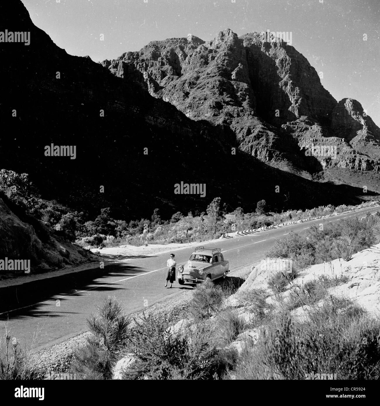 South Africa,1950s. Female stands in front of her car on a deserted road in the outback. Stock Photo