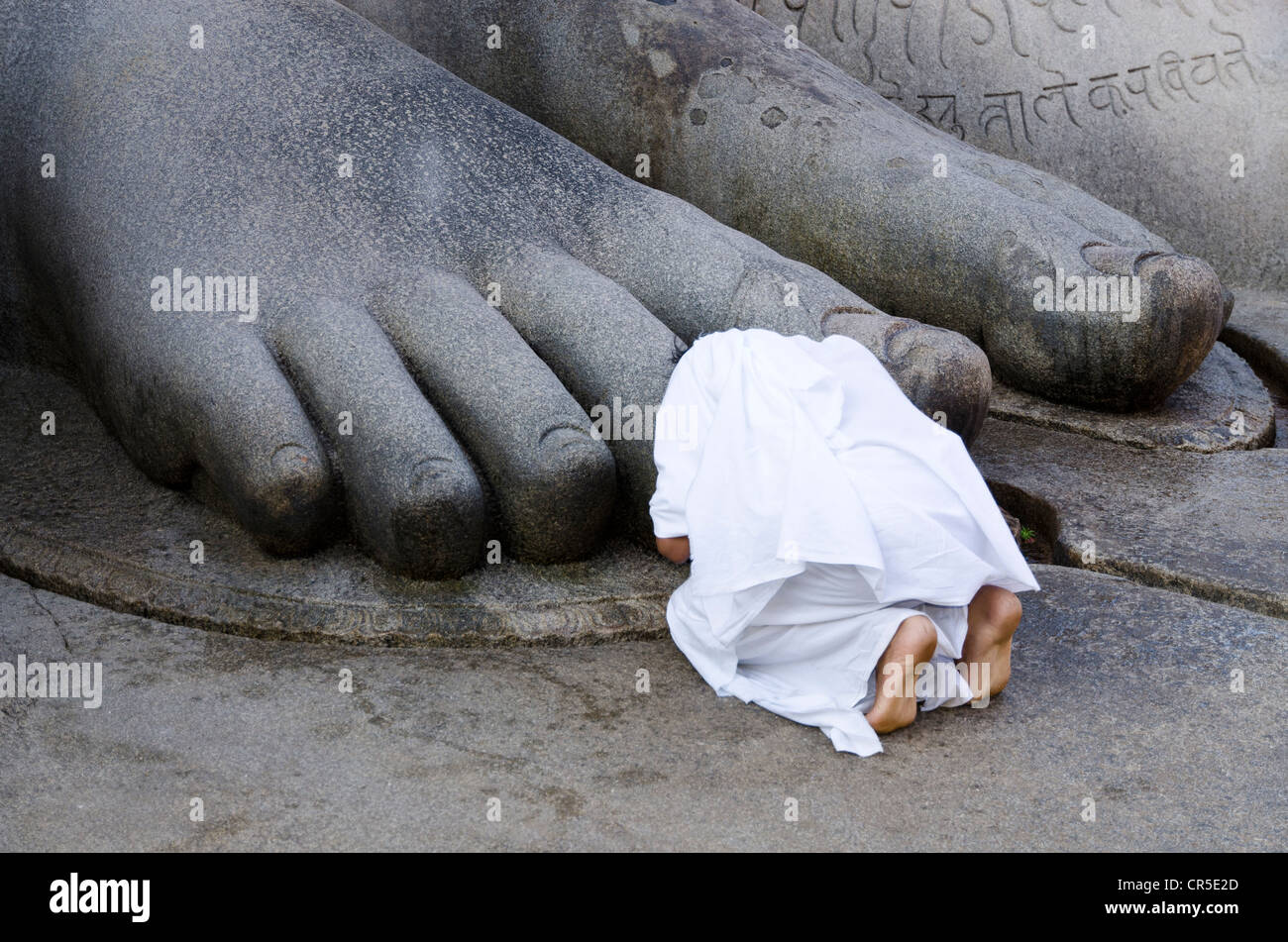 Jain pilgrim is praying at the feet of the gigantic statue of Gomateshwara in Sravanabelagola, Karnataka, India, Asia Stock Photo