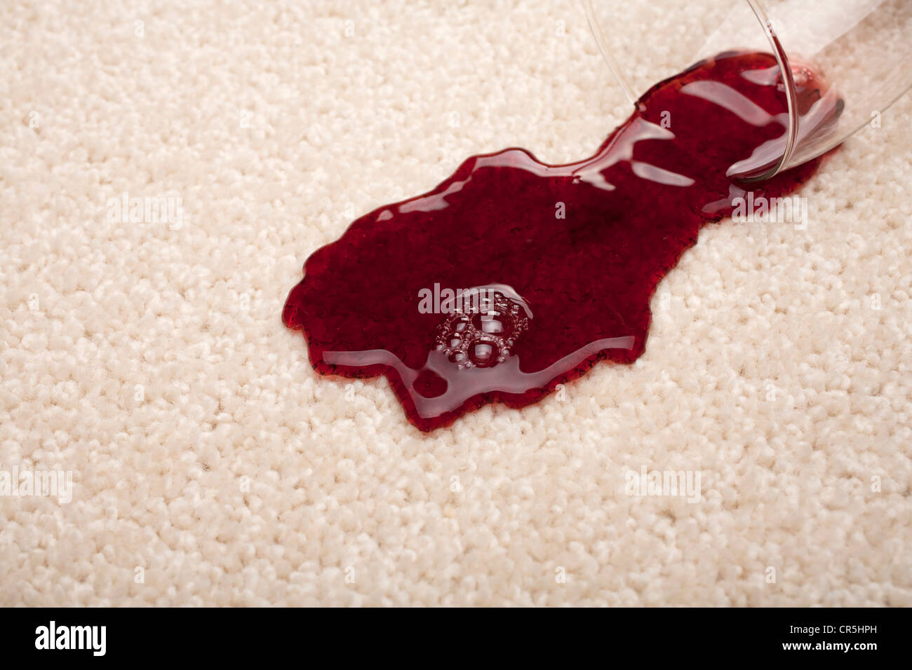 Red wine spilling from a glass onto a light coloured carpet. Stock Photo