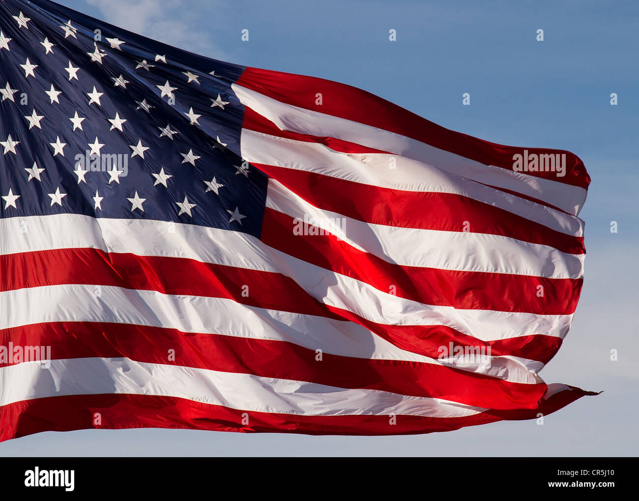 A crisp, brilliant American flag flies in a steady breeze with blue sky ...