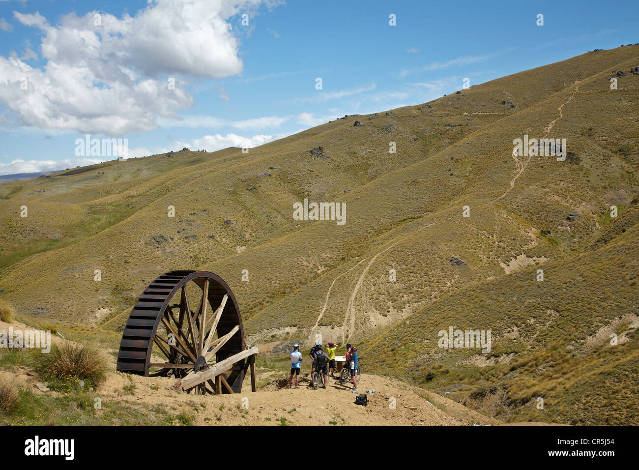 Historic Waterwheel, Young Australian Gold Mine, and mountain bikers, Carrick Range, Central Otago, New Zealand Stock Photo