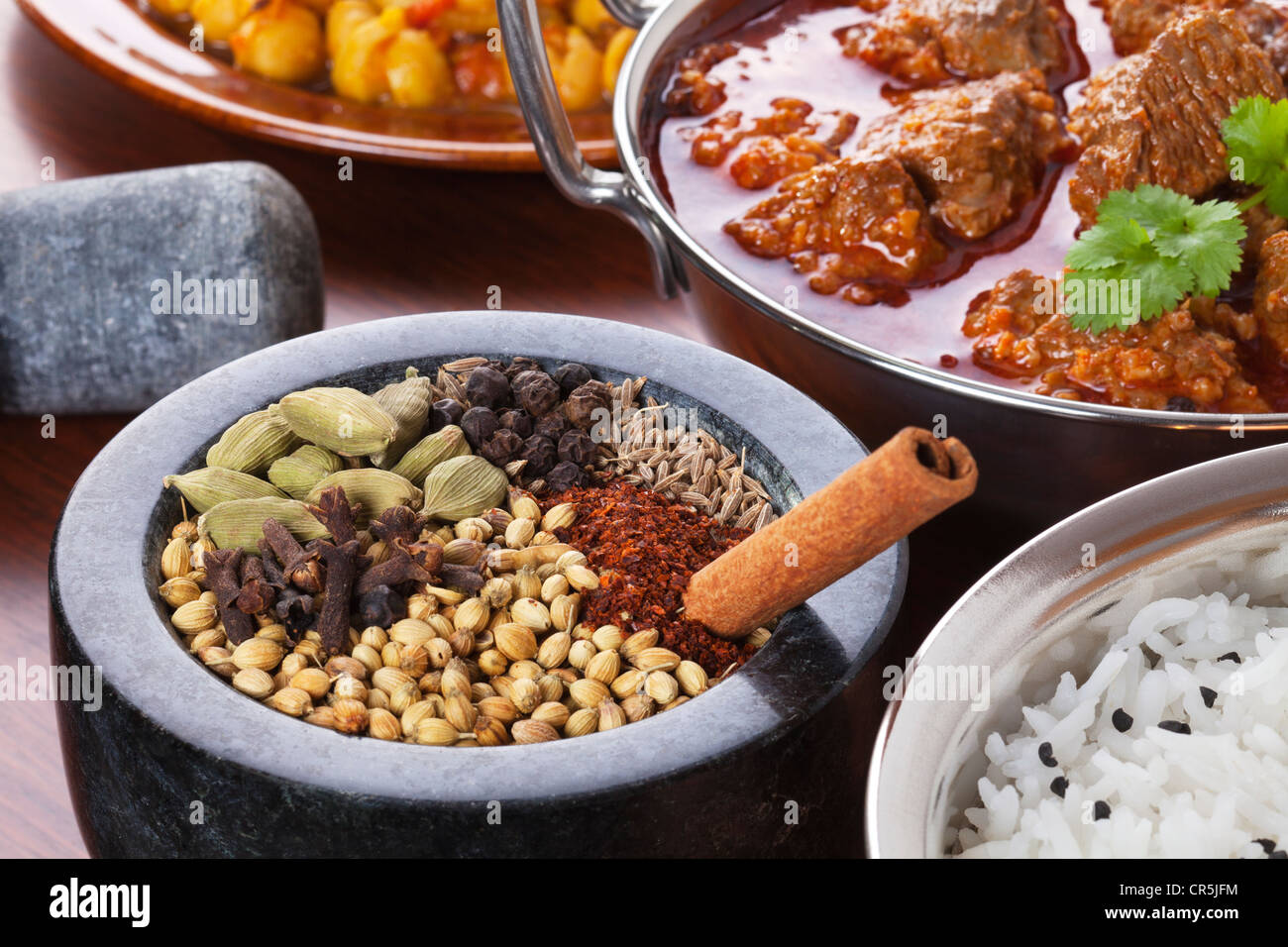 A pestle and mortar full of spices and a bowl of rogan josh lamb curry. Spices are those used in the lamb dish. Stock Photo