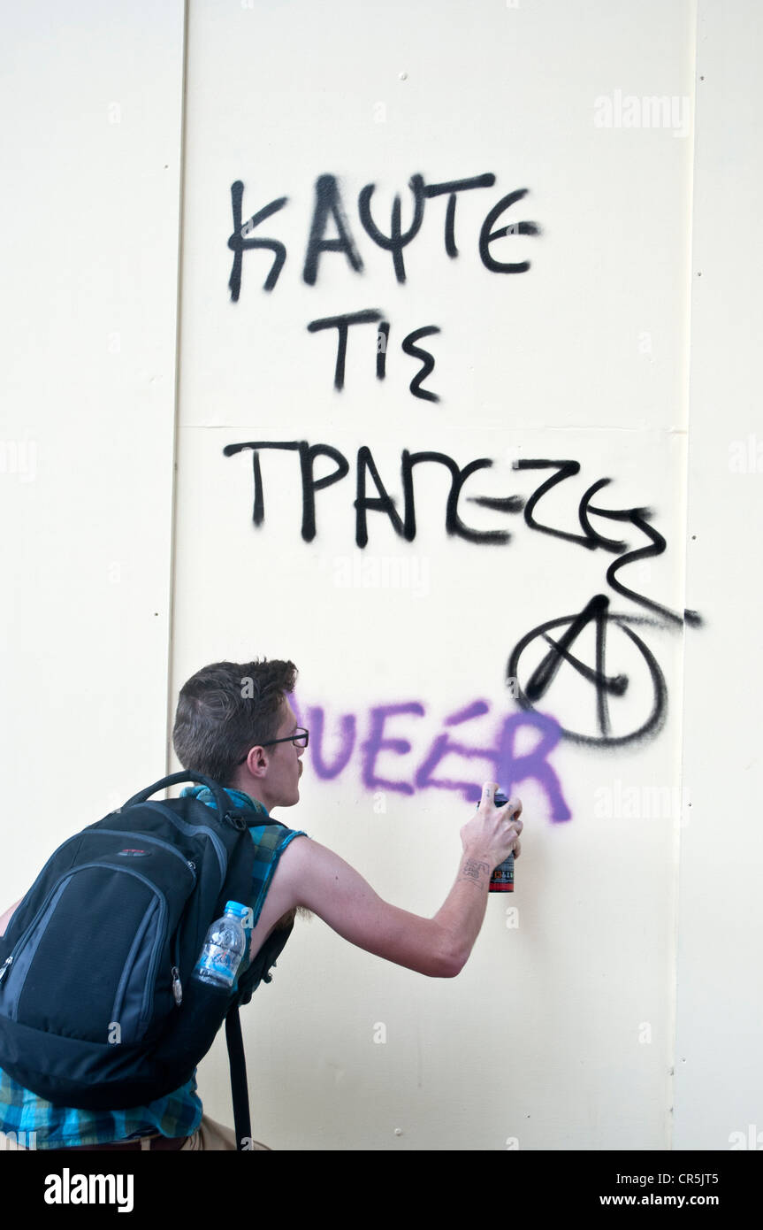 'Burn the banks' graffiti and participant in the Athens, Greece gay parade adding with spray ' queer' Stock Photo