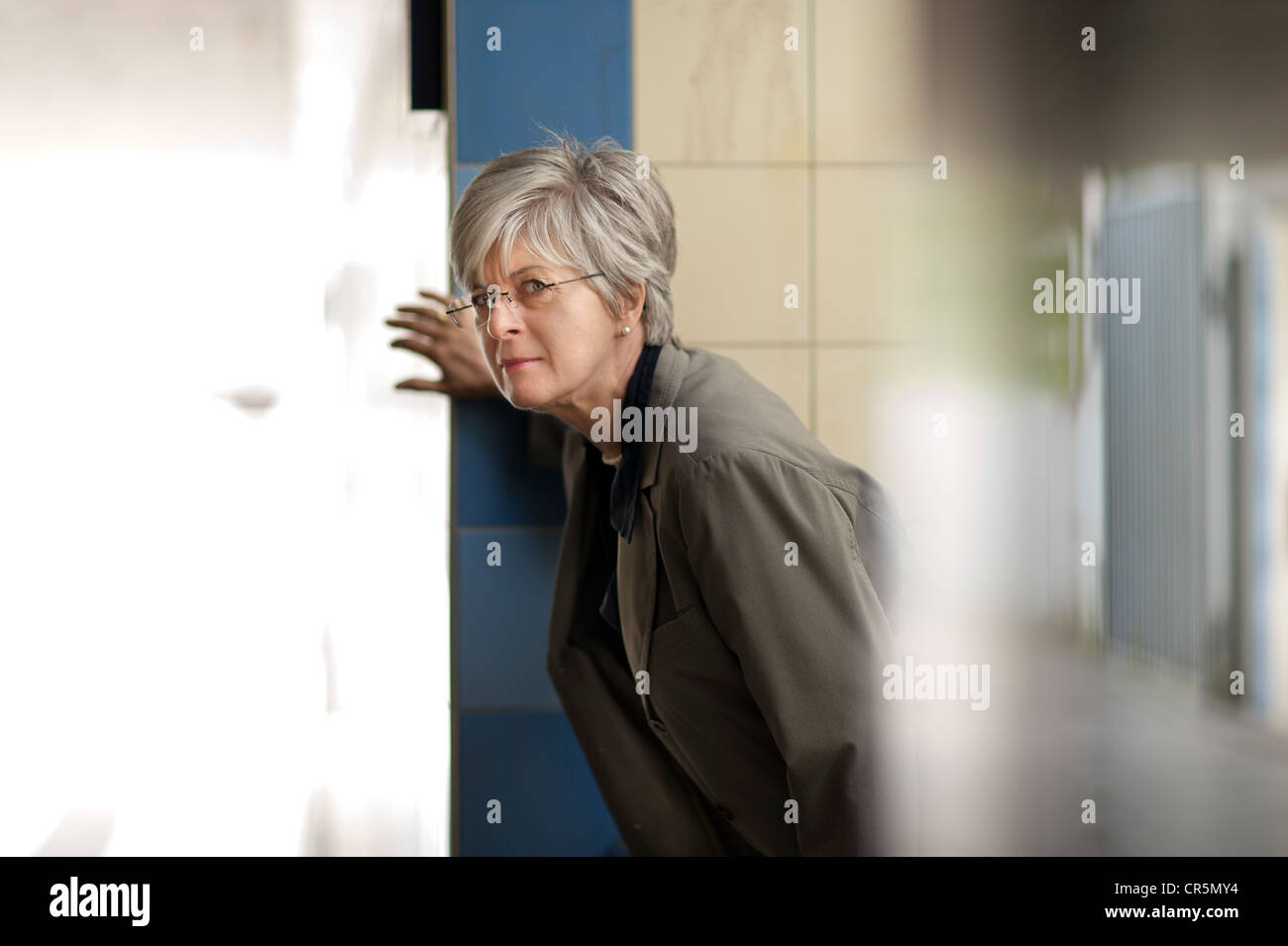 Woman looking carefully around the corner of a staircase Stock Photo