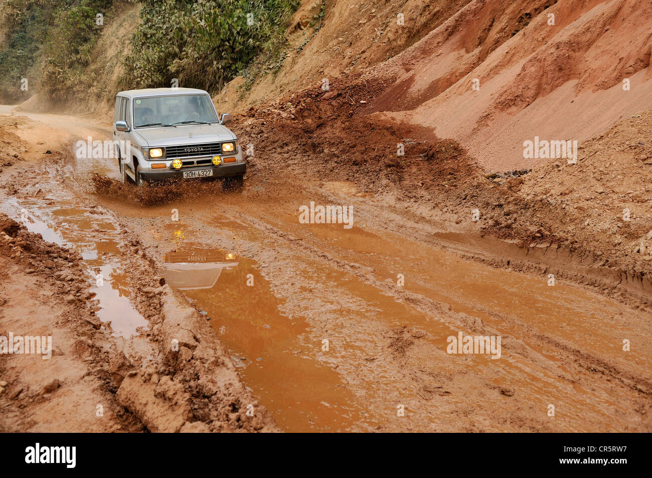 Toyota Land Cruiser driving on a muddy road through puddles, Vietnam, Asia Stock Photo