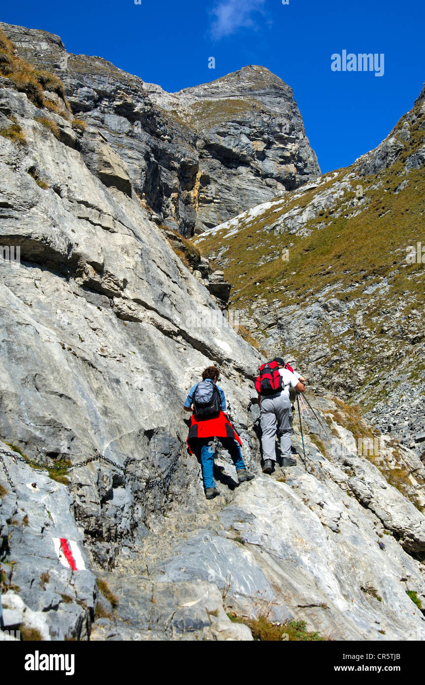 Hikers on a rocky section of the trail secured by metal chains en route to the Laemmerenhuette refuge, Bernese Alps, Switzerland Stock Photo