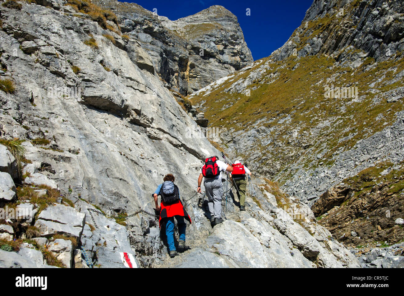 Hikers on a rocky section of the trail secured by metal chains en route to the Laemmerenhuette refuge, Bernese Alps, Switzerland Stock Photo