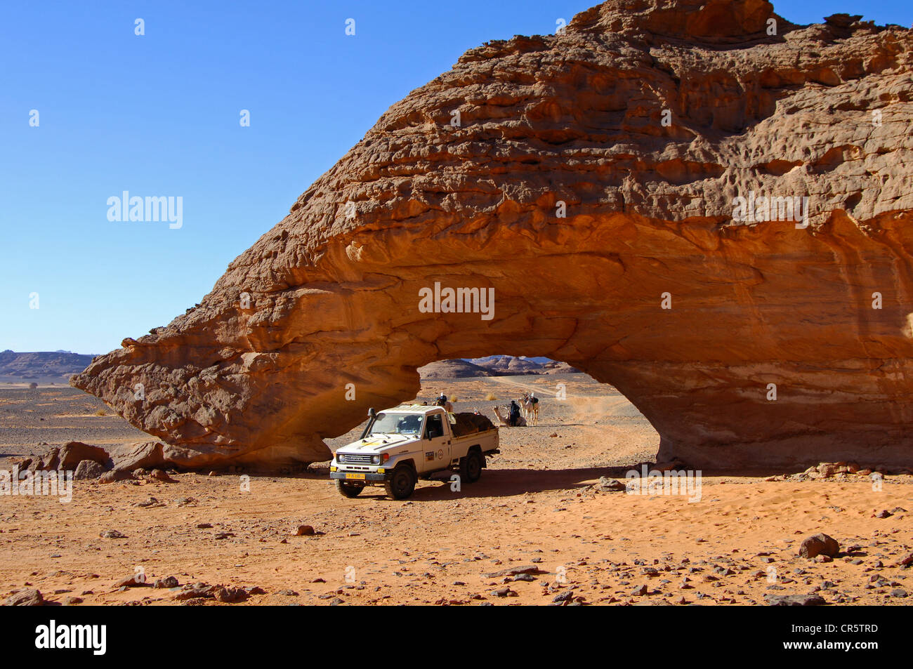 Off-road vehicle driving though a rock arch shaped by wind erosion ...