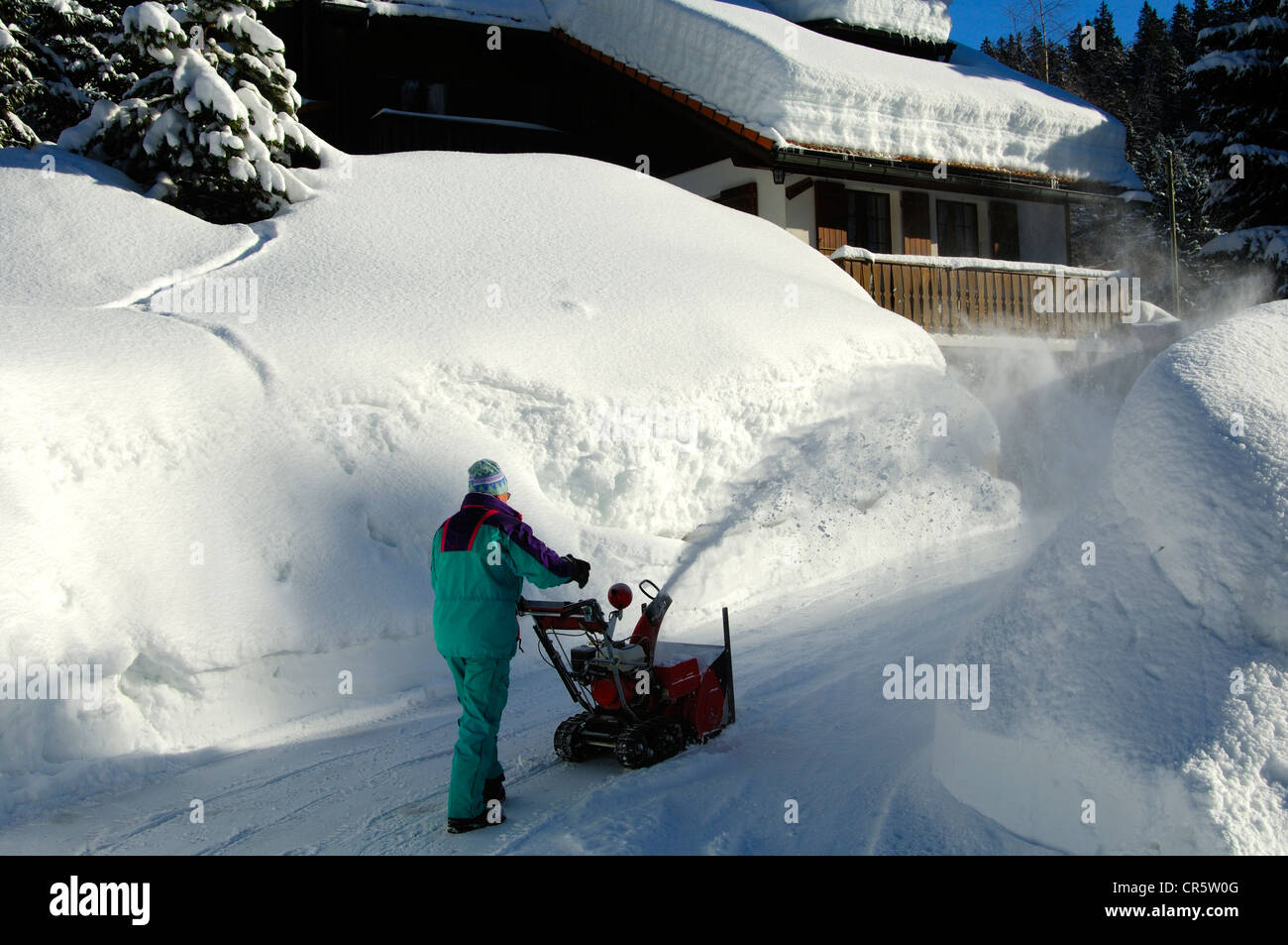 Man clearing snow with a hand snow blower in front of his snow-covered house, Givrine, St. Cergue, Jura, Switzerland, Europe Stock Photo