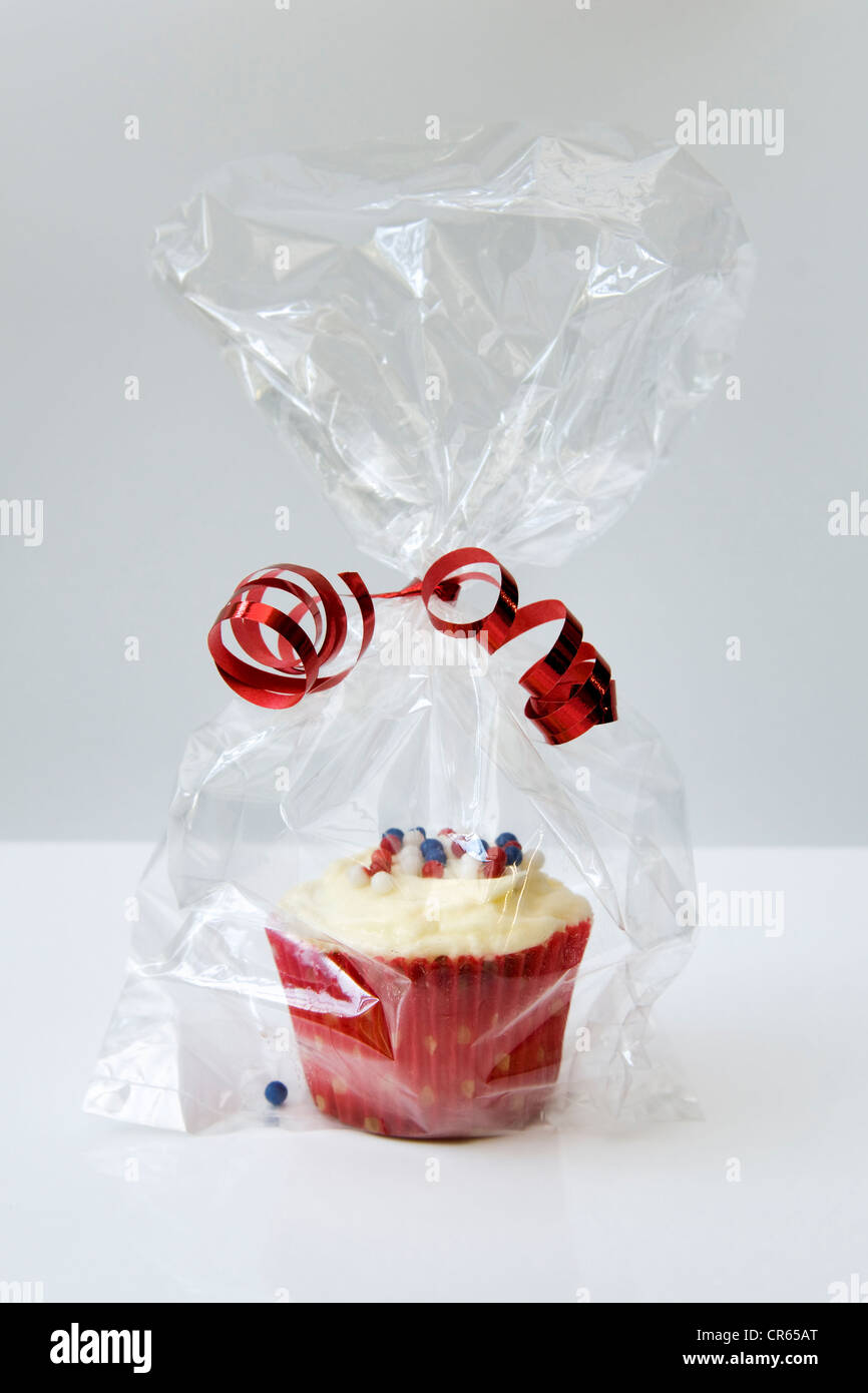 Cupcake in a colourful red wrapper and cellophane bag tied with a red ribbon against a white background Stock Photo