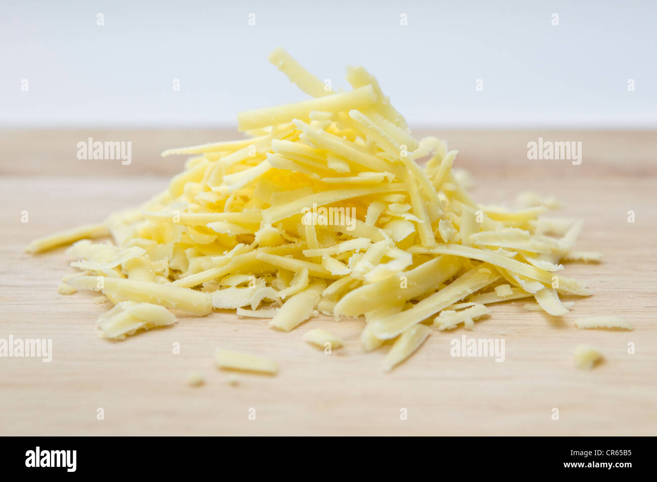 Grated cheese on wooden chopping board against white background Stock Photo