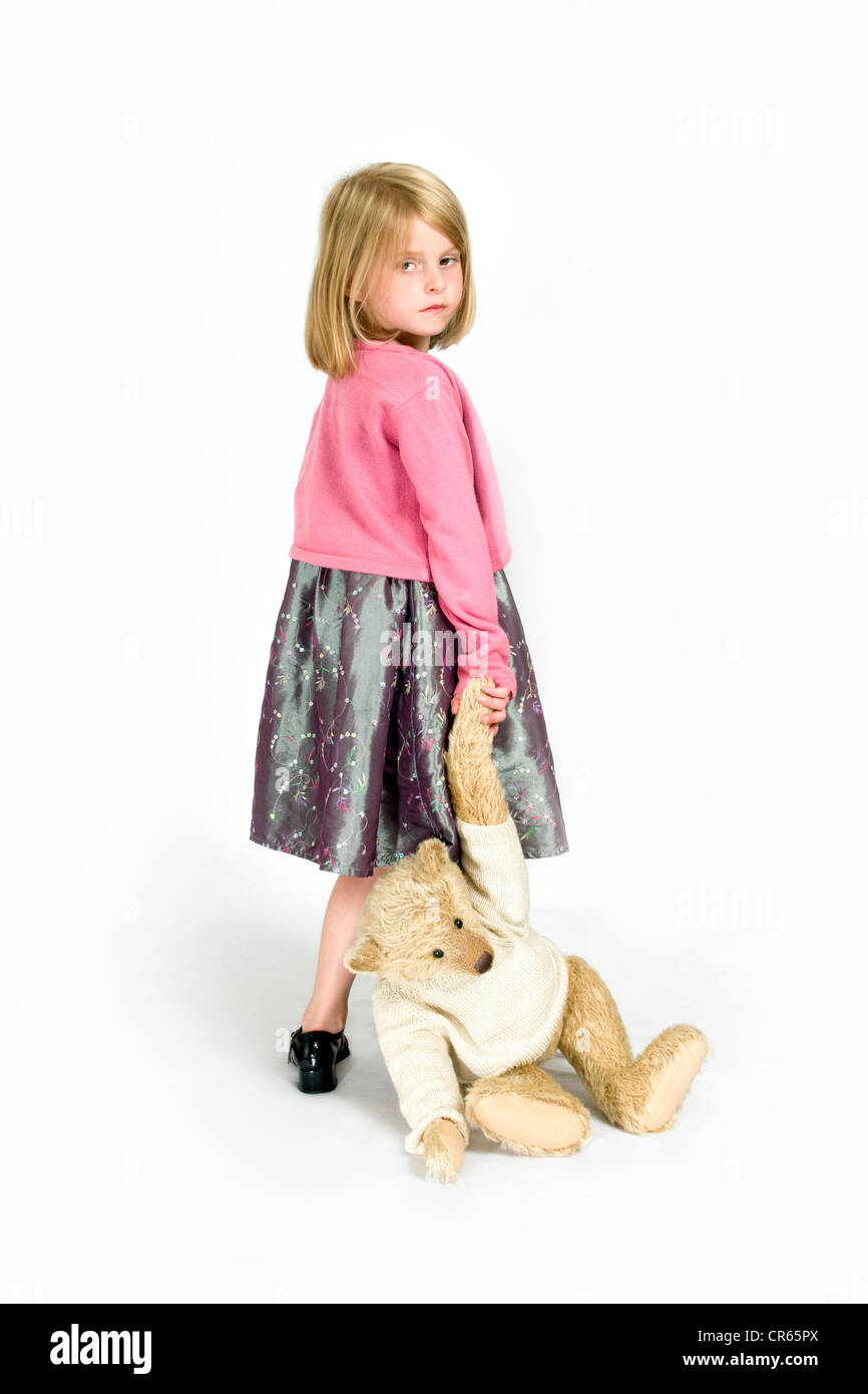 Studio image of an unhappy Caucasian 7 year old girl dragging a teddy bear on a white background, concept of naughty child Stock Photo