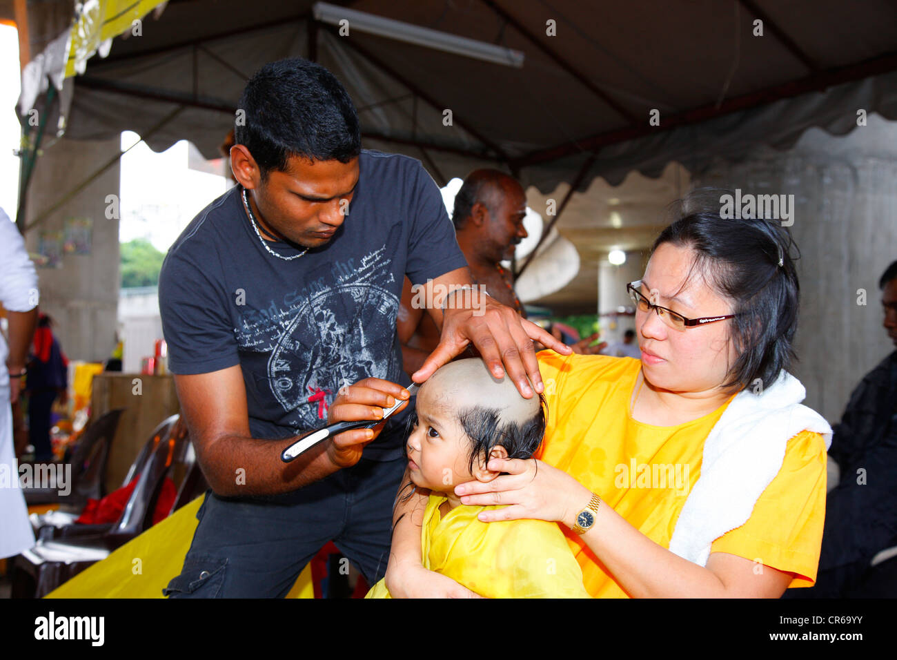 Child's hair being shaved with a razor, Hindu festival Thaipusam, Batu Caves limestone caves and temples, Kuala Lumpur, Malaysia Stock Photo