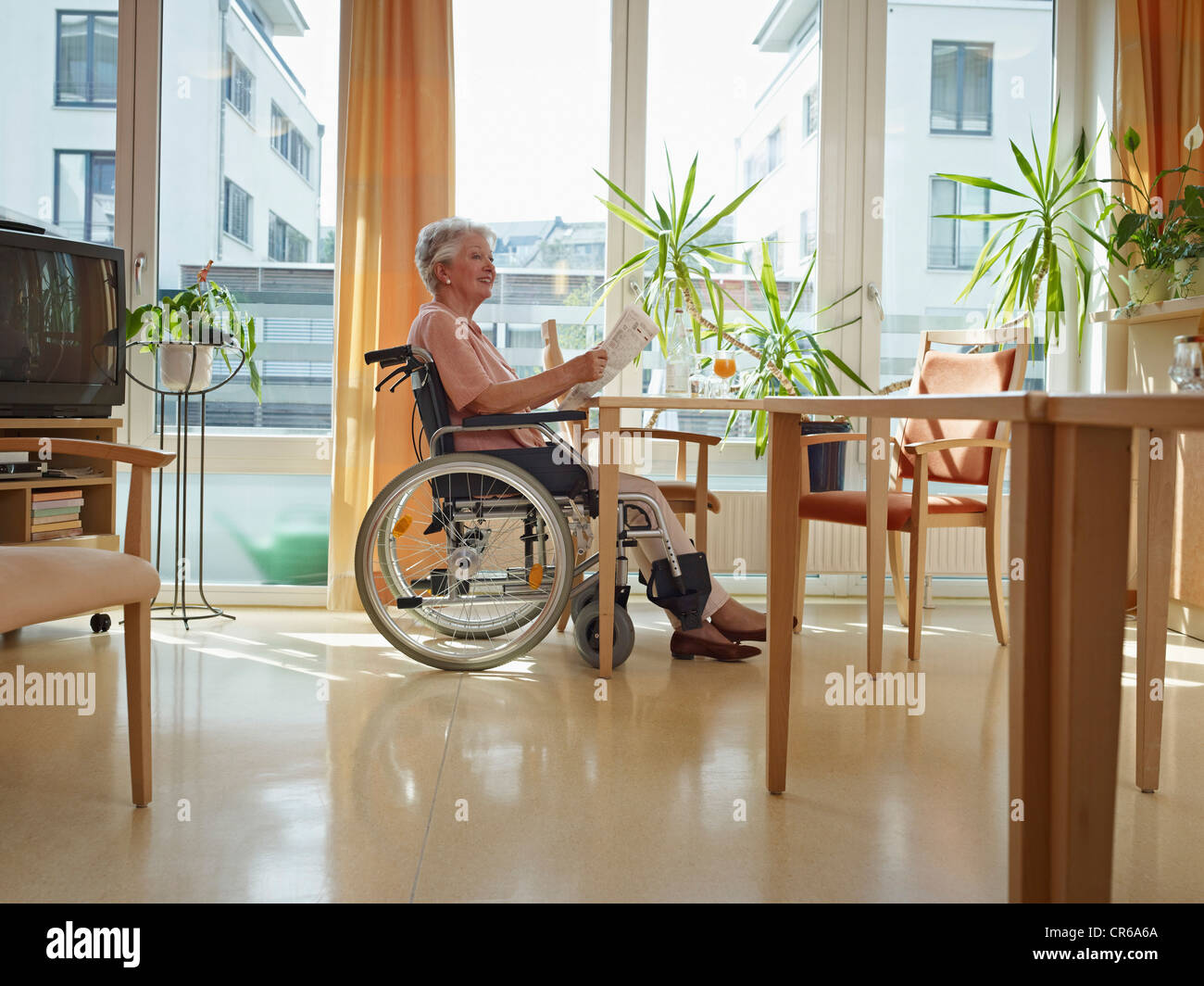 Germany, Cologne, Senior woman reading newspaper in nursing home Stock Photo
