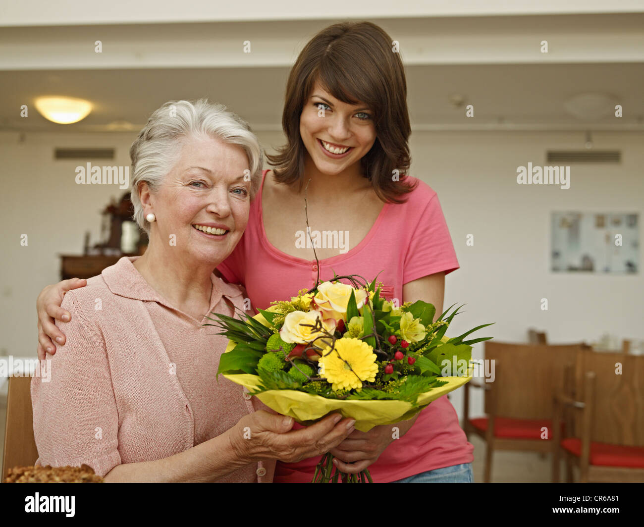 Germany, Cologne, Women holding bouquet in nursing home, smiling, portrait Stock Photo