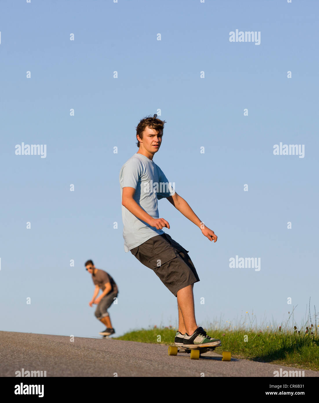 Austria, Young men doing longboarding on road Stock Photo