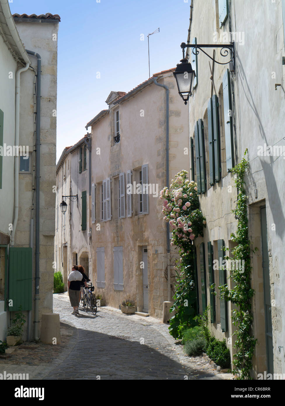 France, Ile de Re, St Martin de Re, pretty old back street with couple with bicycles, lamp and roses Stock Photo