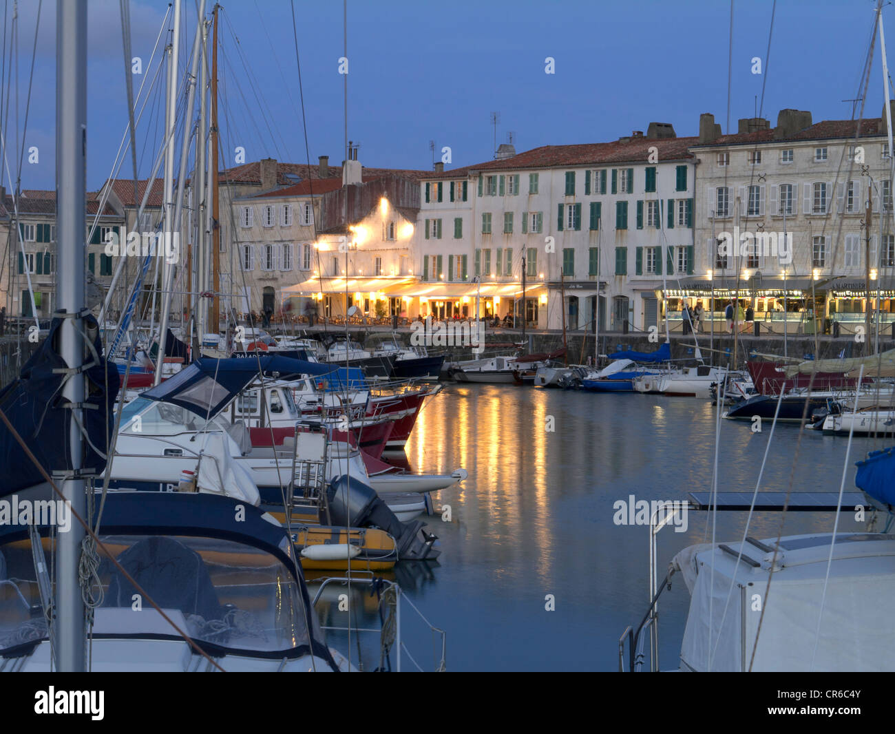 France, Ile de Re, St Martin de Re, harbour towards town and restaurants with boats in foreground at dusk Stock Photo