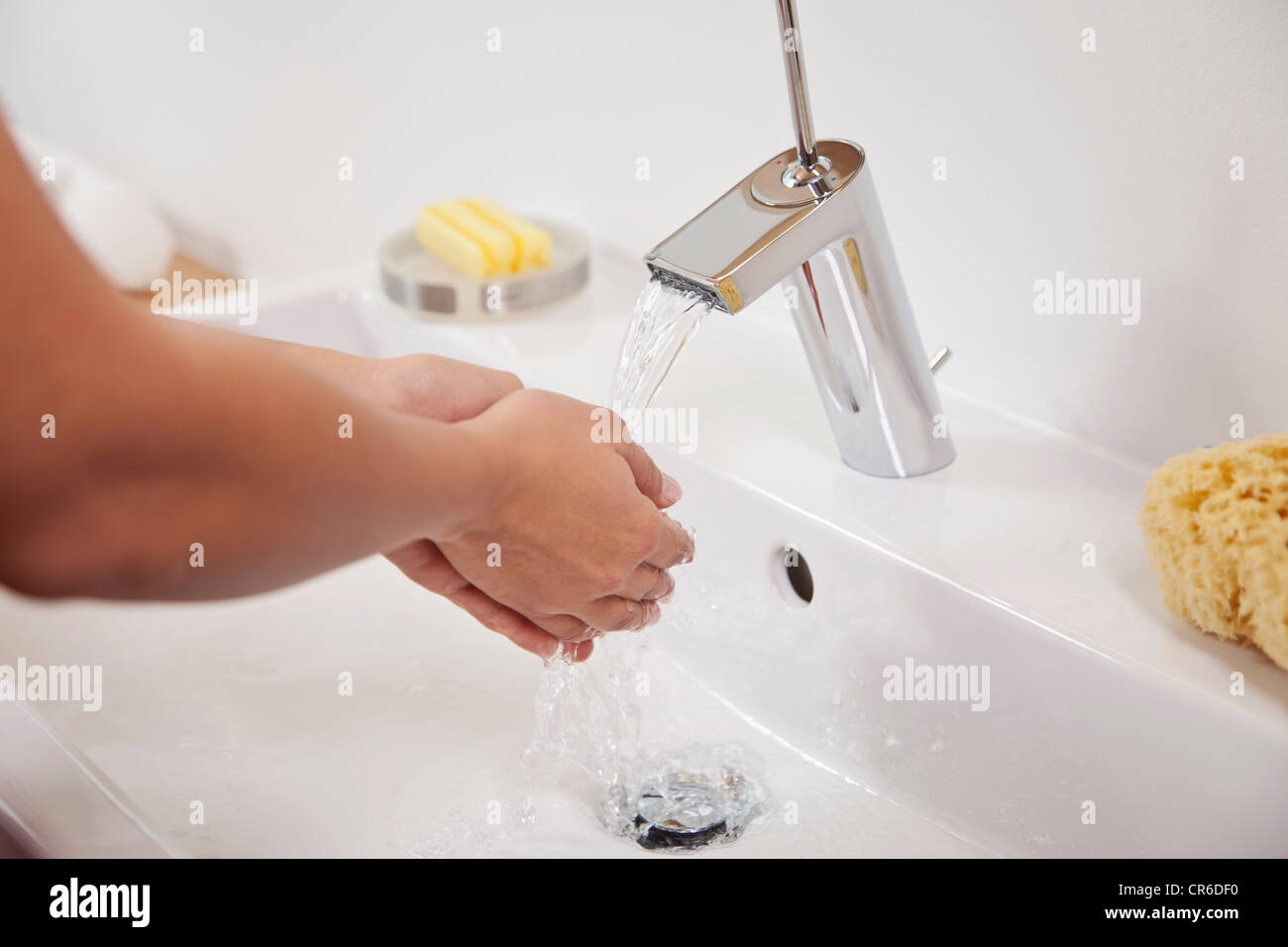 Germany, Bavaria, Young woman washing hands in bathroom sink Stock Photo