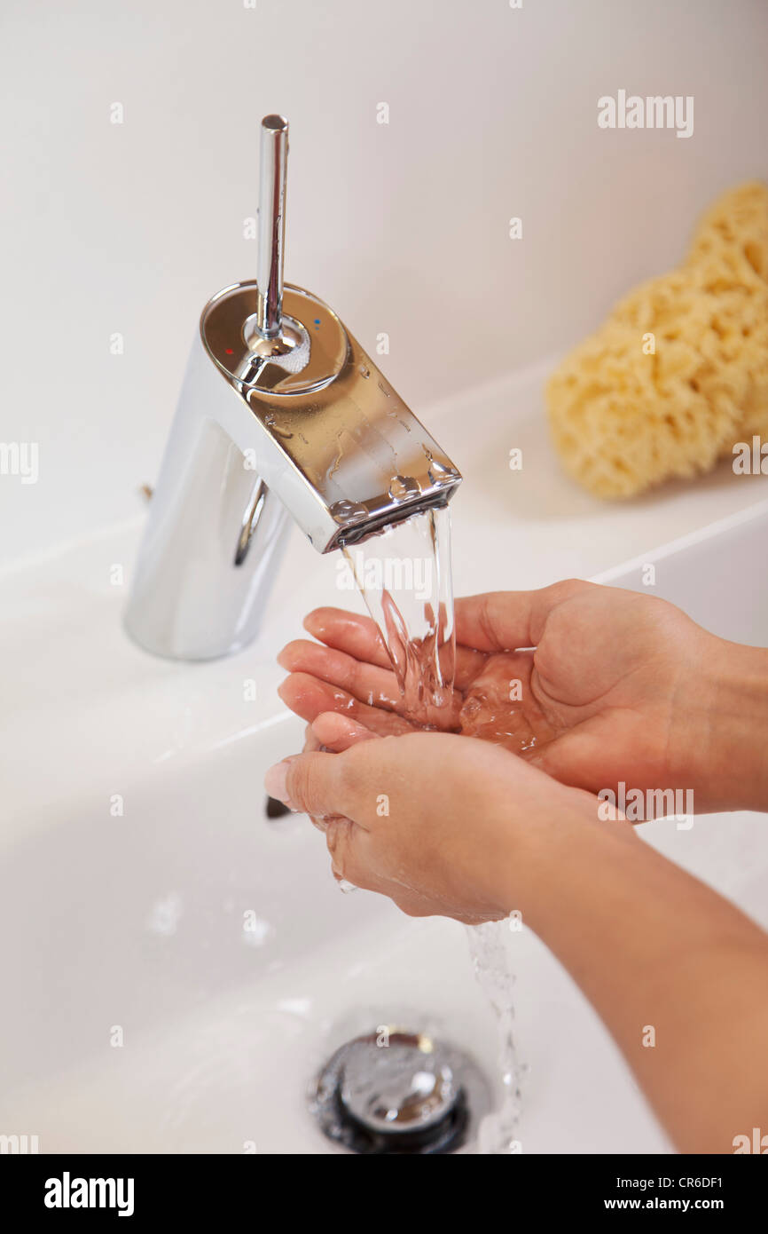 Germany, Bavaria, Young woman washing hands in bathroom sink Stock