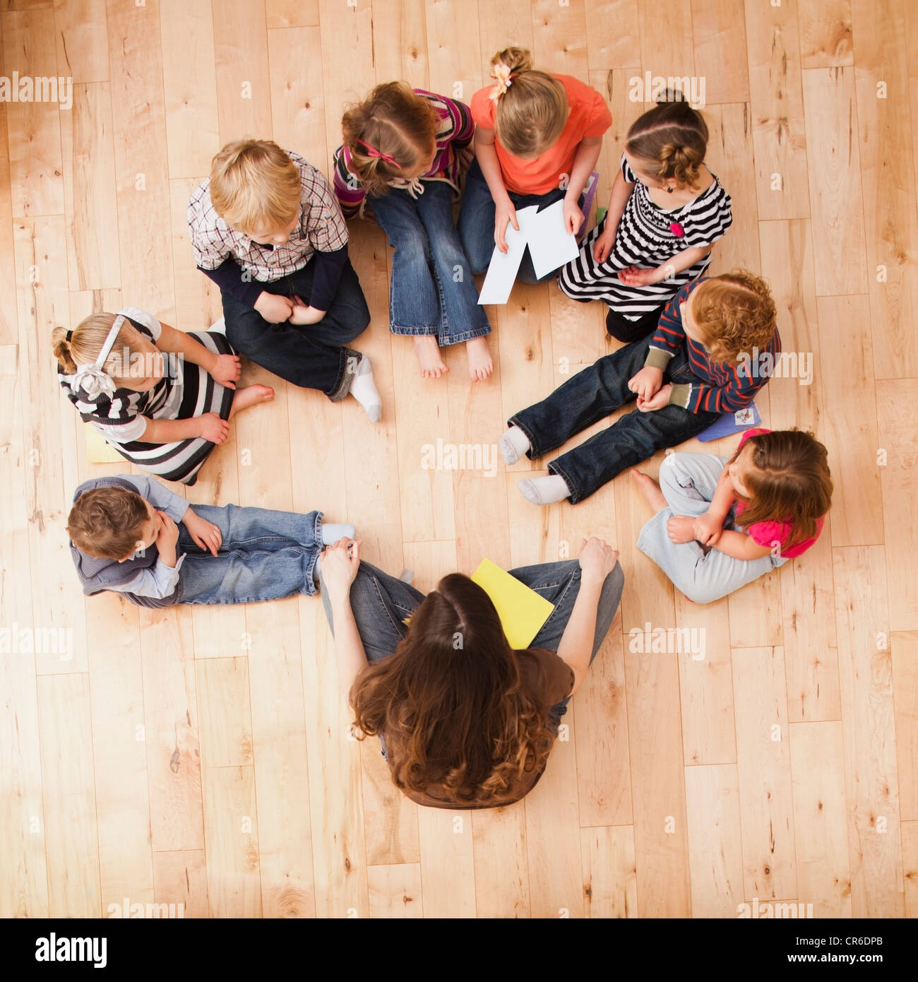 Children (2-3, 4-5) sitting in circle around teacher, directly above Stock Photo