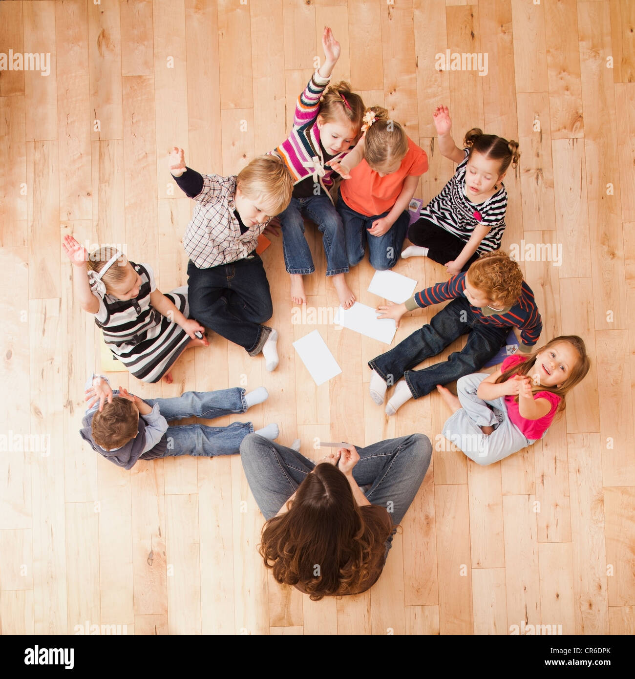 Children (2-3, 4-5) sitting on floor and raising hands, directly above Stock Photo