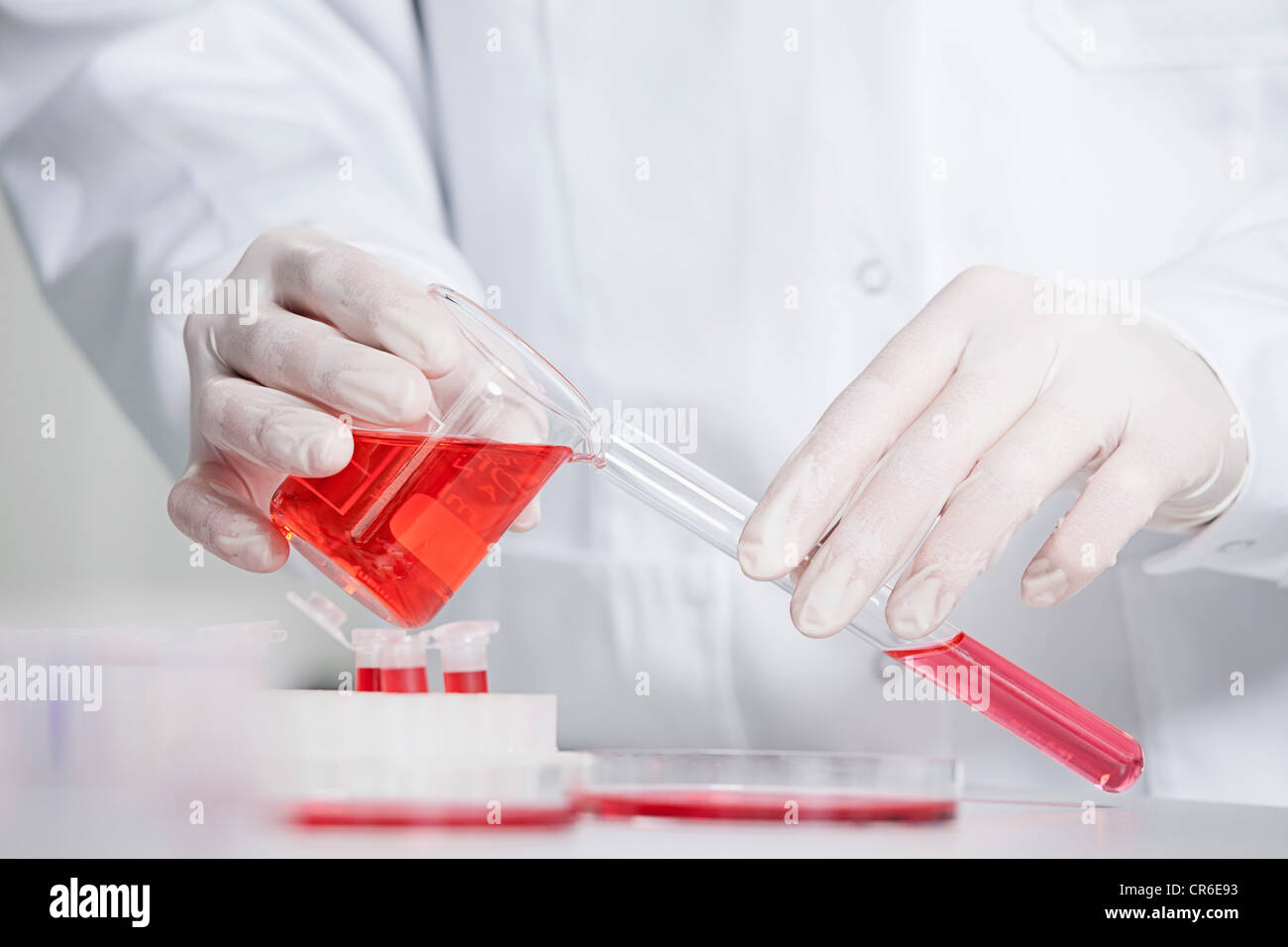 Germany, Bavaria, Munich, Scientist pouring red liquid in test tube for medical research in laboratory Stock Photo