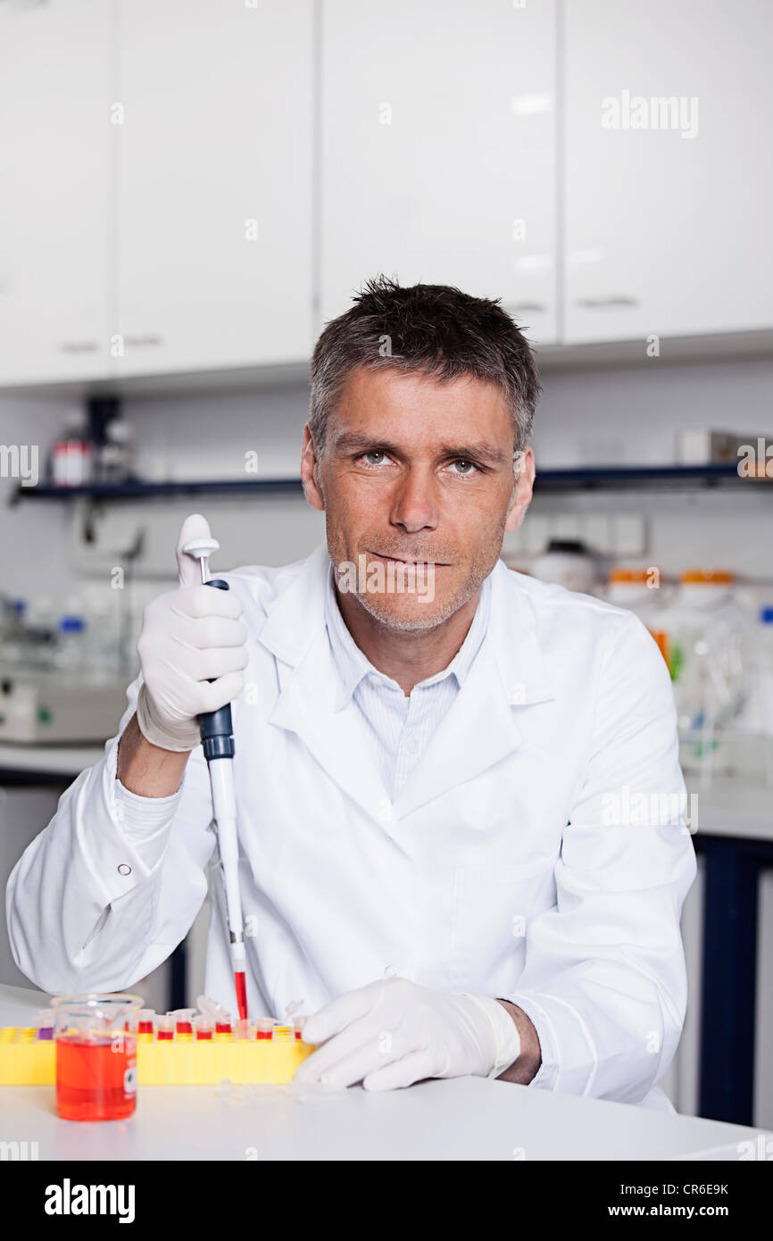 Germany, Bavaria, Munich, Scientist pouring red liquid with pipette for medical research in laboratory Stock Photo