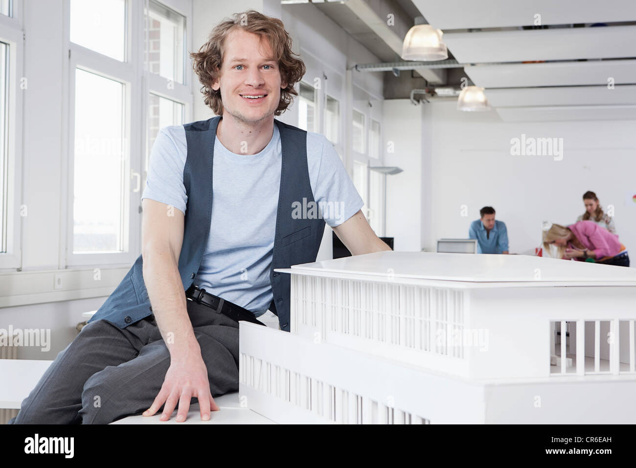 Germany, Bavaria, Munich, Architect with architectural model, colleagues working in background Stock Photo
