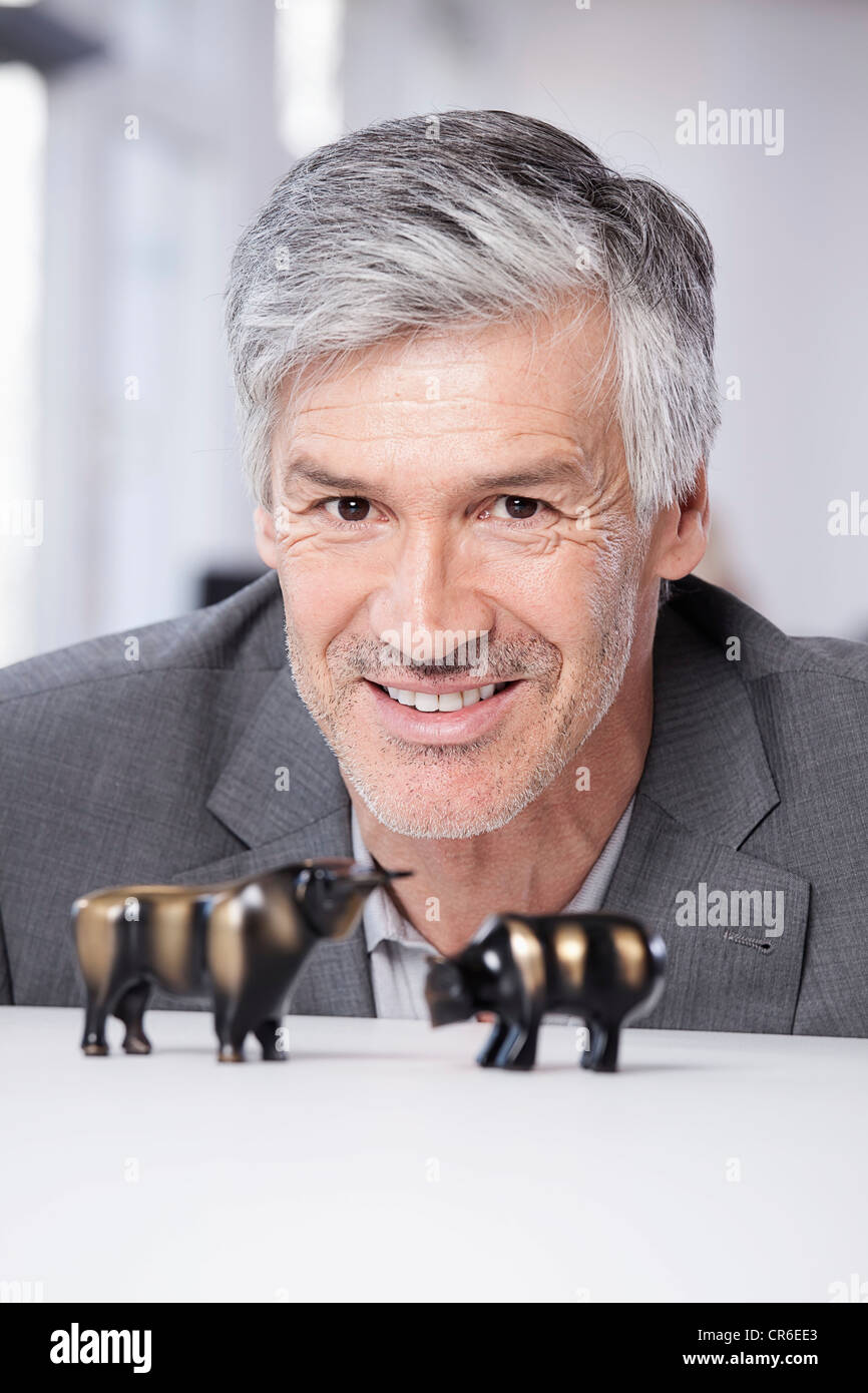 Germany, Bavaria, Munich, Mature man with bull and bear figurines, smiling, portrait Stock Photo