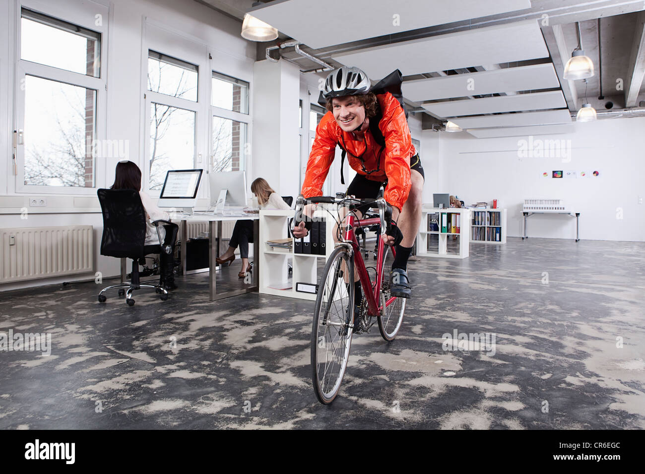 Germany, Bavaria, Munich, Courier man cycling in office, colleagues working Stock Photo
