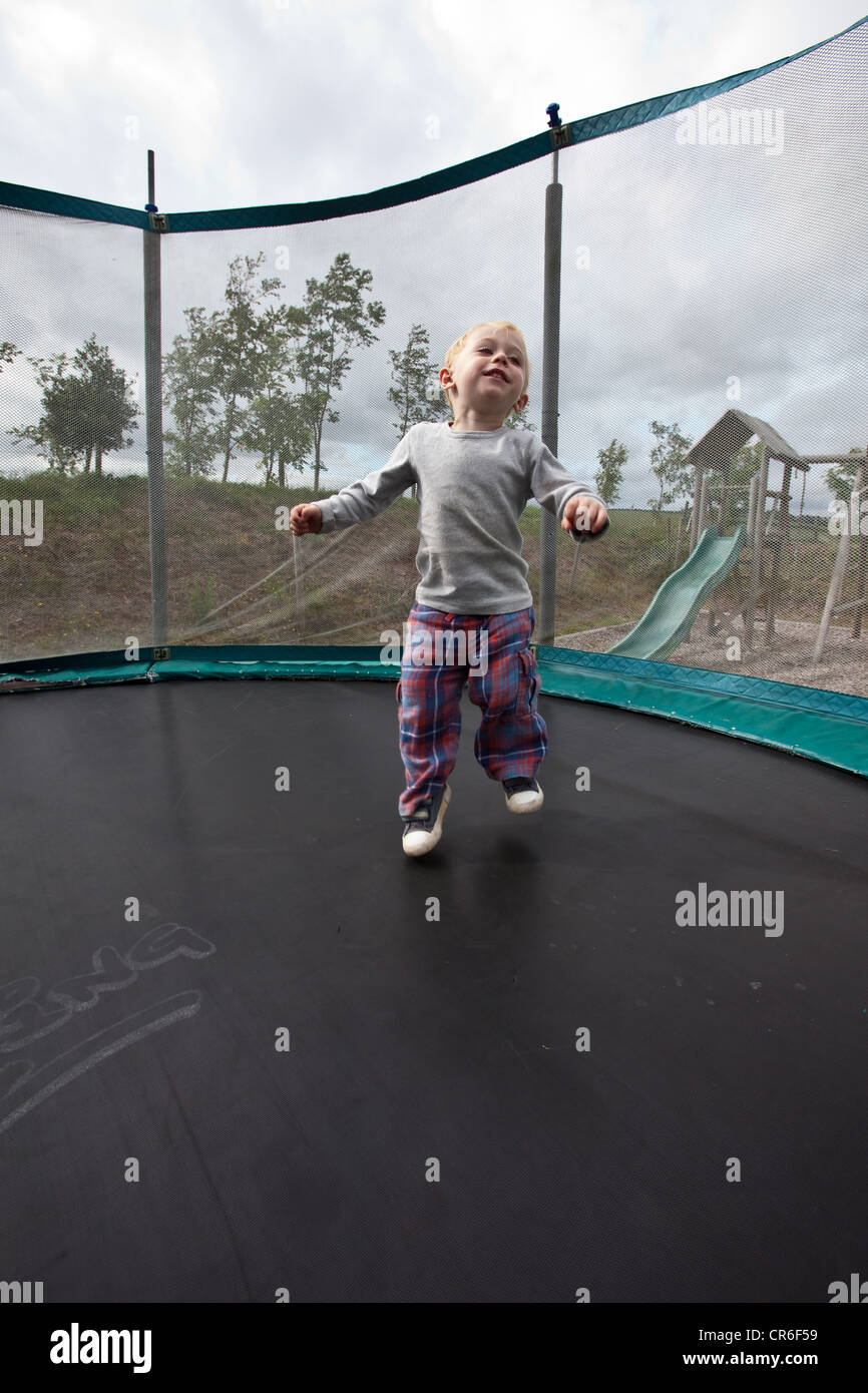 Two year old boy bouncing on a garden trampoline, Devon, england