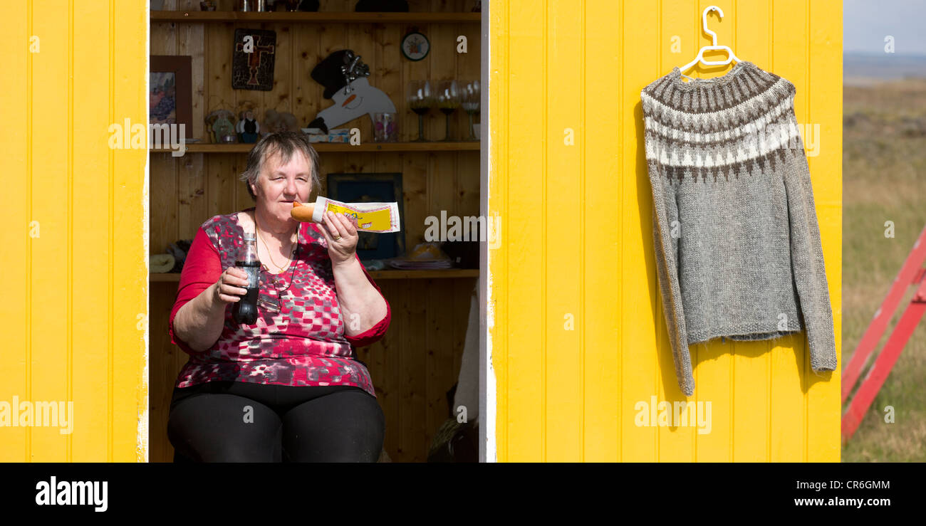 Owner of  small countryside shop enjoying a hot dog and soda, handmade wool sweater for sale, South Coast Iceland Stock Photo