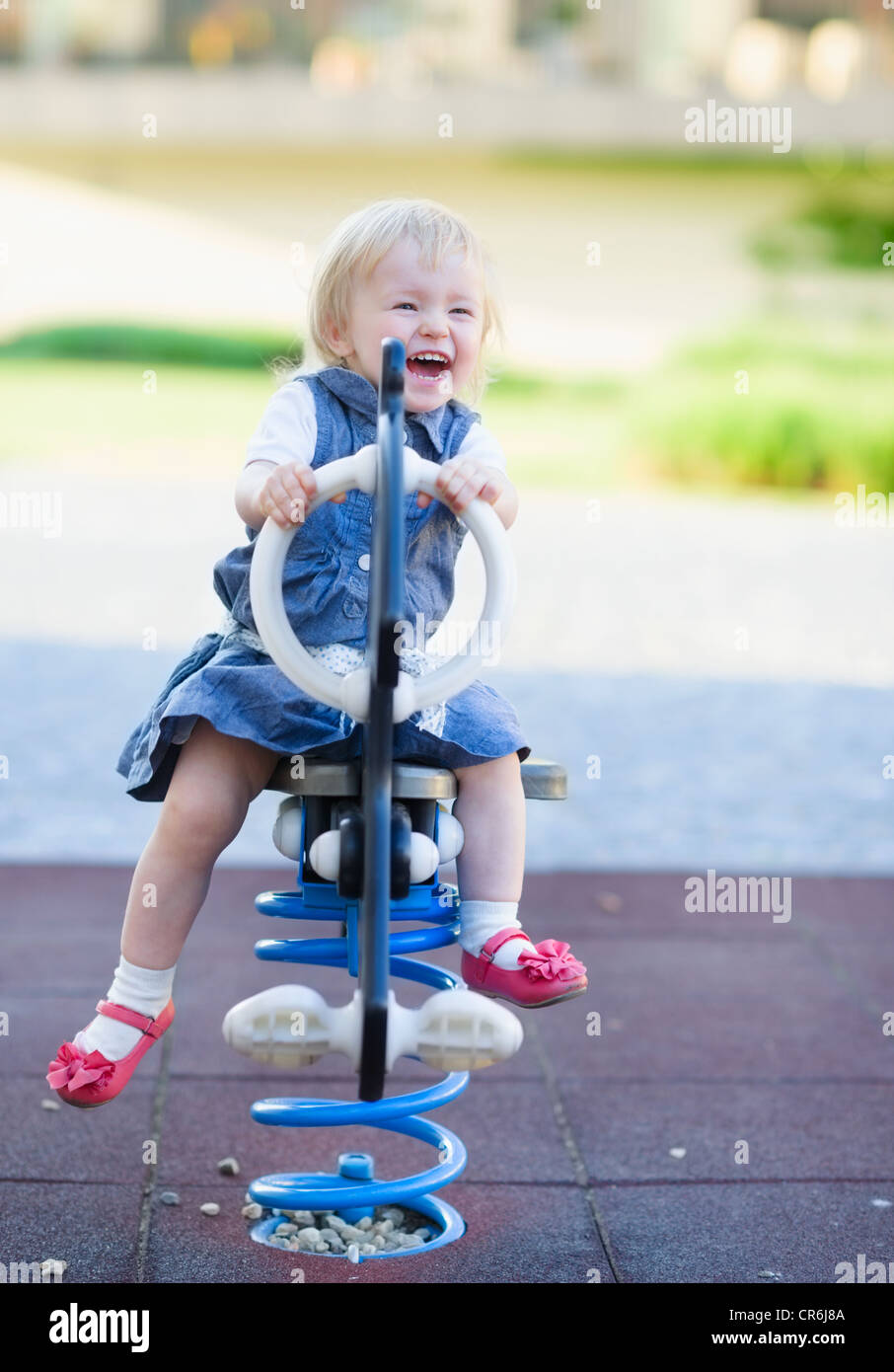 Happy baby swinging on horse on playground Stock Photo