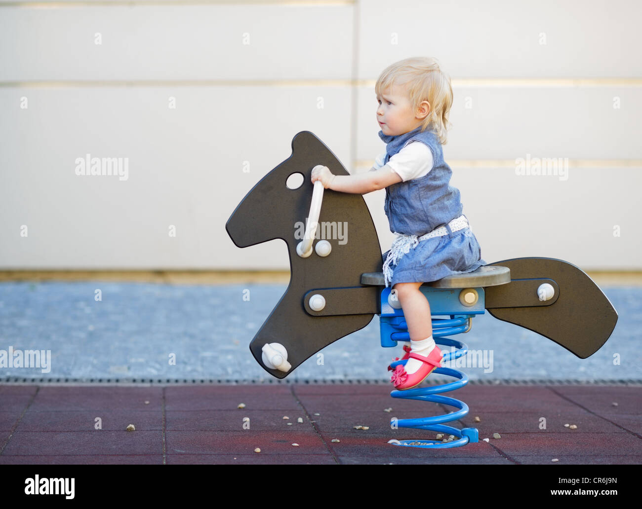 Happy baby swinging on horse on playground. Side view Stock Photo