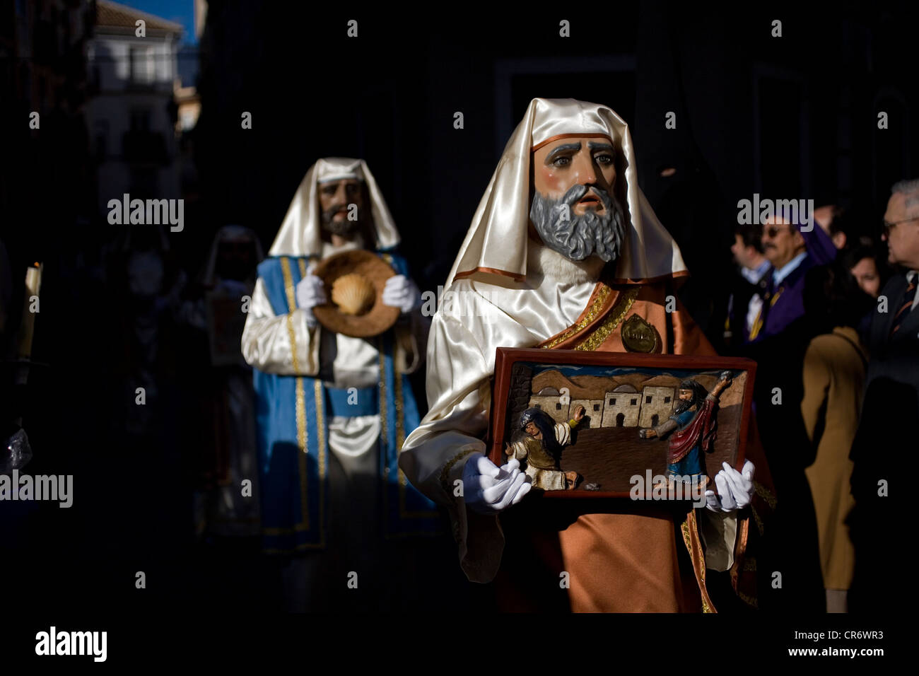 Masked men dressed as biblical characters walk through the street holding miniatures during an Easter Holy Week procession Stock Photo