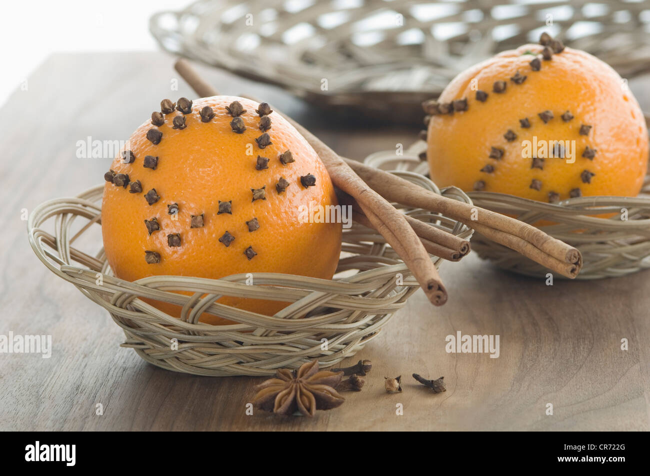 Orange studded with cloves and cinnamon stick in basket besides star anise on table Stock Photo