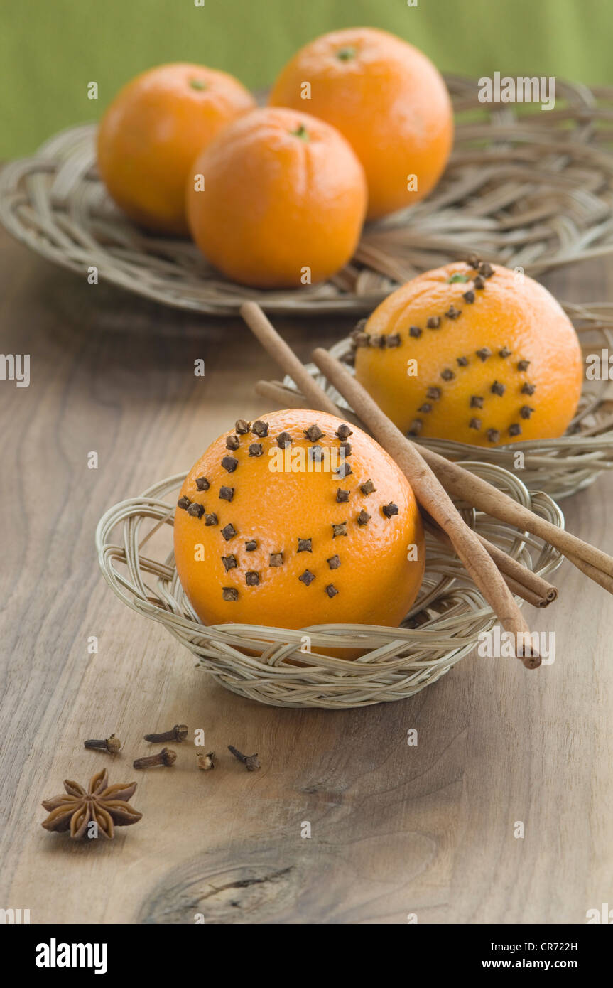 Orange studded with cloves and cinnamon stick in basket besides star anise on table Stock Photo