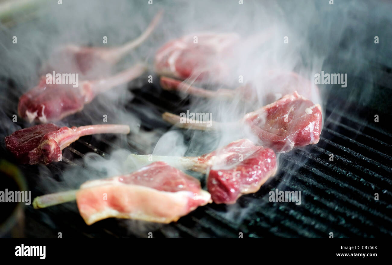 lamb chops cooking on barbecue grill with smoke Stock Photo