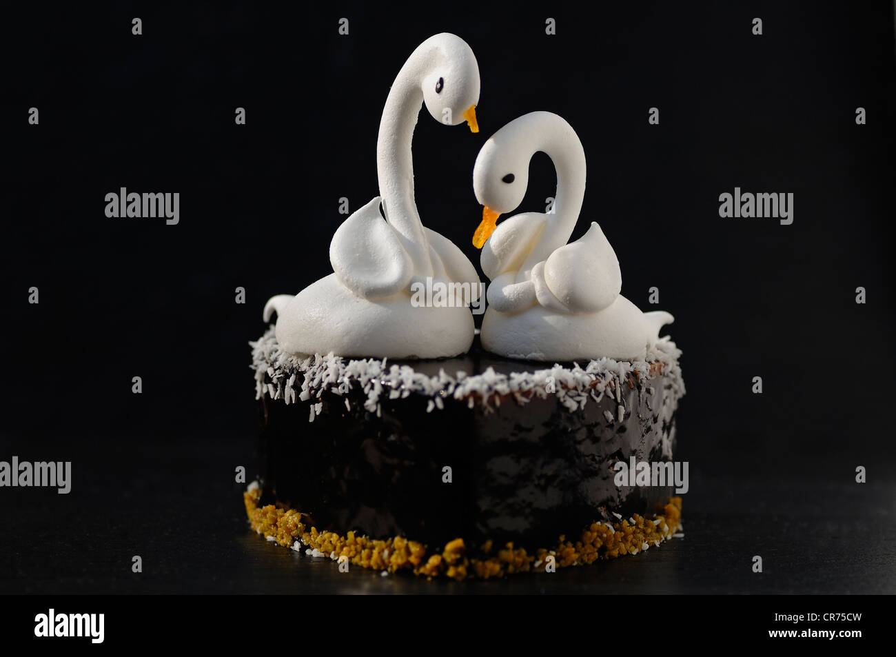 Two meringue swans on a chocolate heart, beaks made from apricots, on a slate in a patisserie Stock Photo