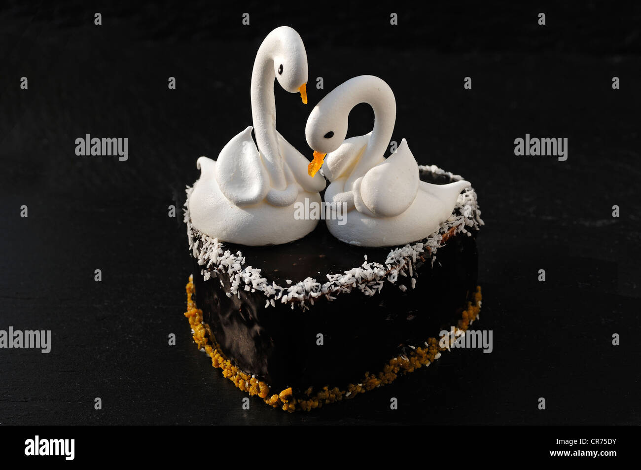 Two meringue swans on a chocolate heart, beaks made from apricots, on a slate in a patisserie Stock Photo