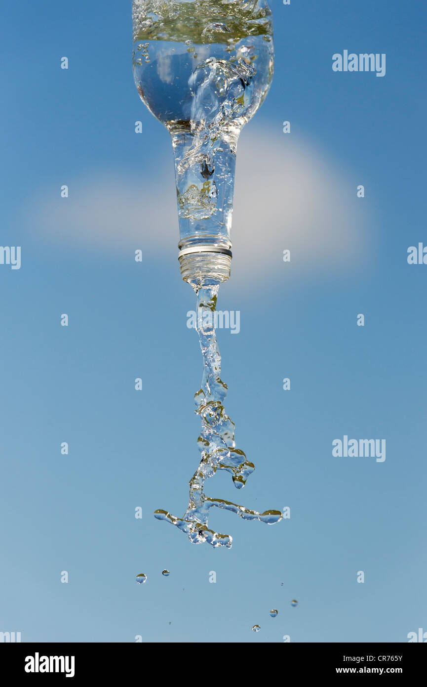 Pouring drinking water from a glass bottle against a blue sky Stock Photo
