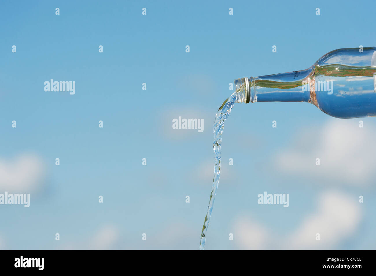 Pouring drinking water from a glass bottle against a blue sky Stock Photo