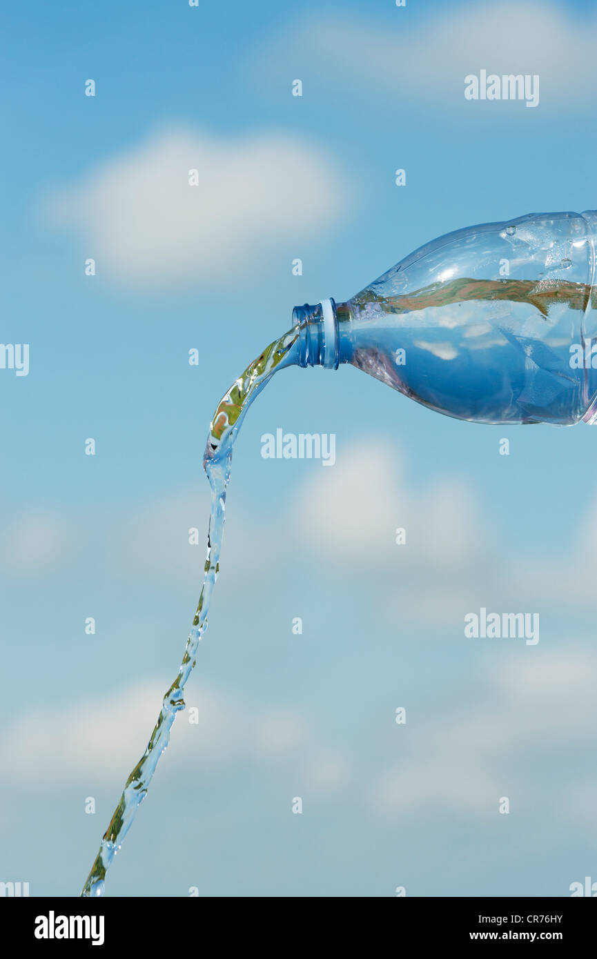 Pouring drinking water from a plastic bottle against a blue sky Stock Photo