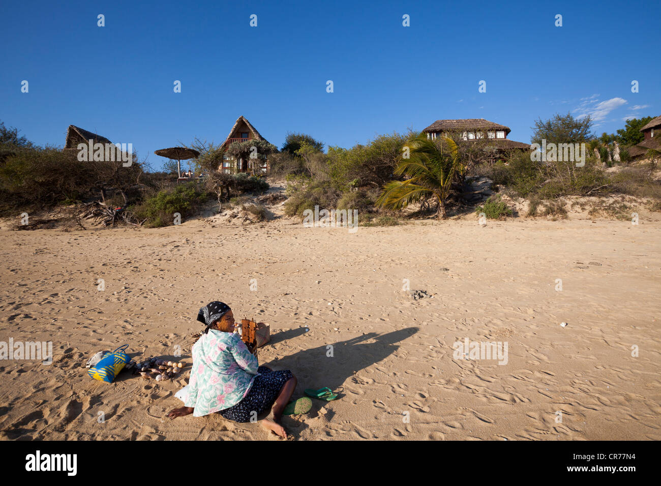 Malagasy woman selling sea shells on beach in front of chalets of Paradisier luxury hotel, Ifaty, Madagascar Stock Photo
