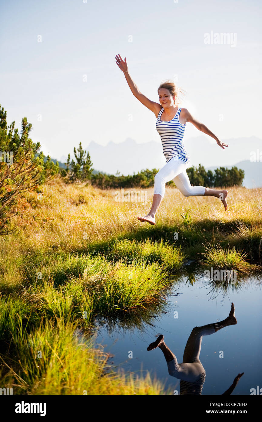 Austria, Salzburg County, Young woman jumping over mountain lake Stock Photo