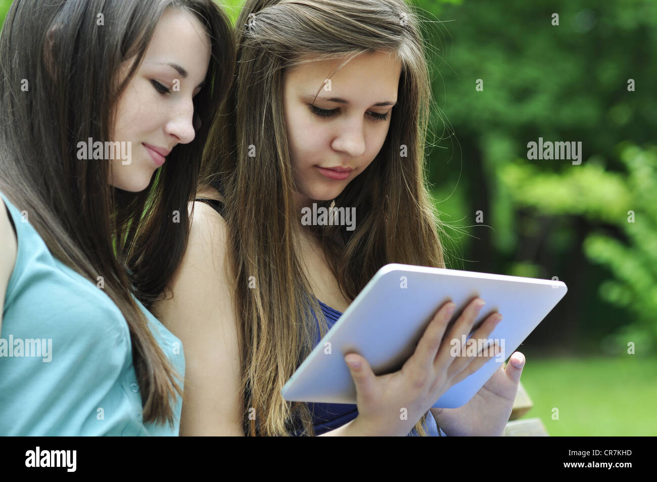 two young girls on bench using a tablet computer outdoor in park Stock ...