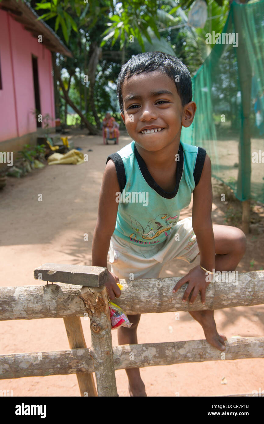 Smiling boy climbing on a fence with their mother sitting behind, Kanjippadom, near Alappuzha (Alleppey), Kerala, India Stock Photo